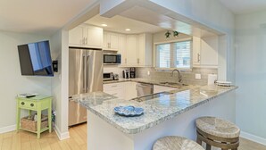 A modern kitchen with a central island, stainless steel appliances, and a flat-screen TV mounted on the wall. - Unit #215 Sand Cay Beach Resort Gulf View (Longboat Key)