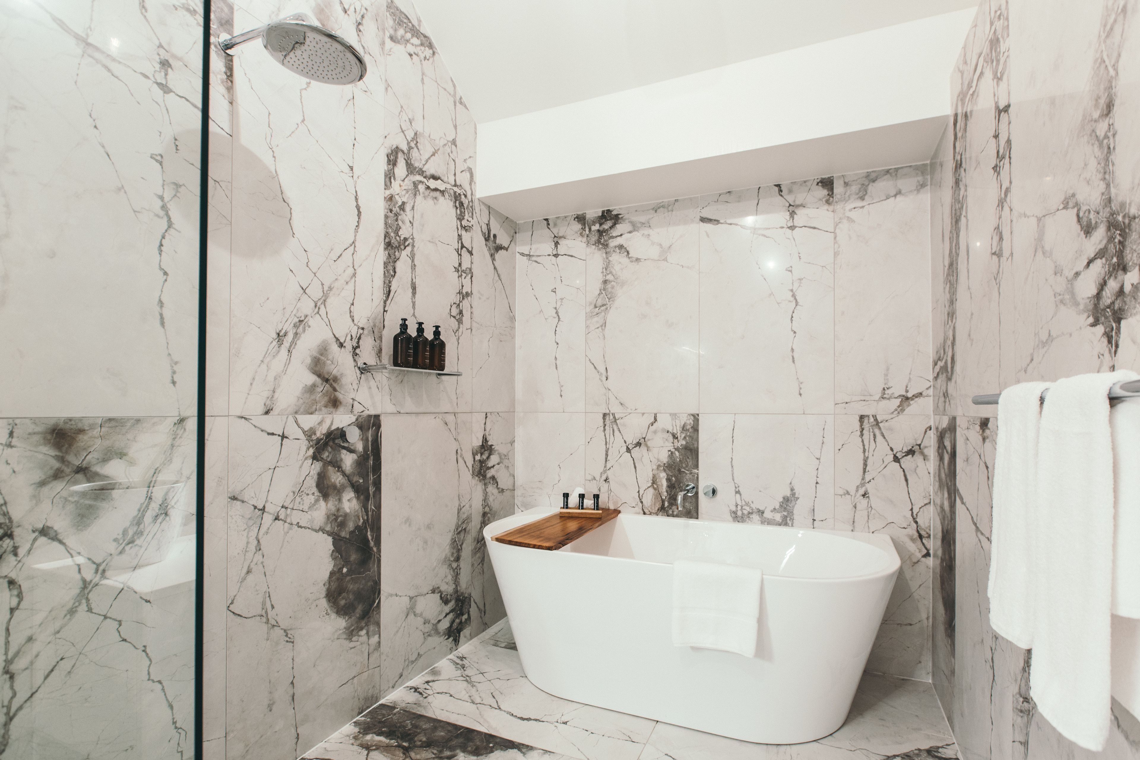 A modern bathroom with a freestanding bathtub, marble walls, and a glass shower enclosure.