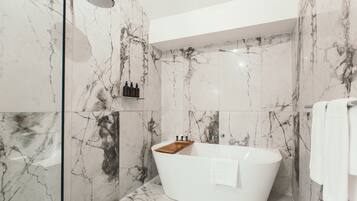 A modern bathroom with a freestanding bathtub, marble walls, and a glass shower enclosure.