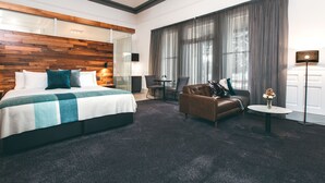 A modern hotel room with a large bed, a leather sofa, a small table, and a desk. - Maylands Lodge (New Town)