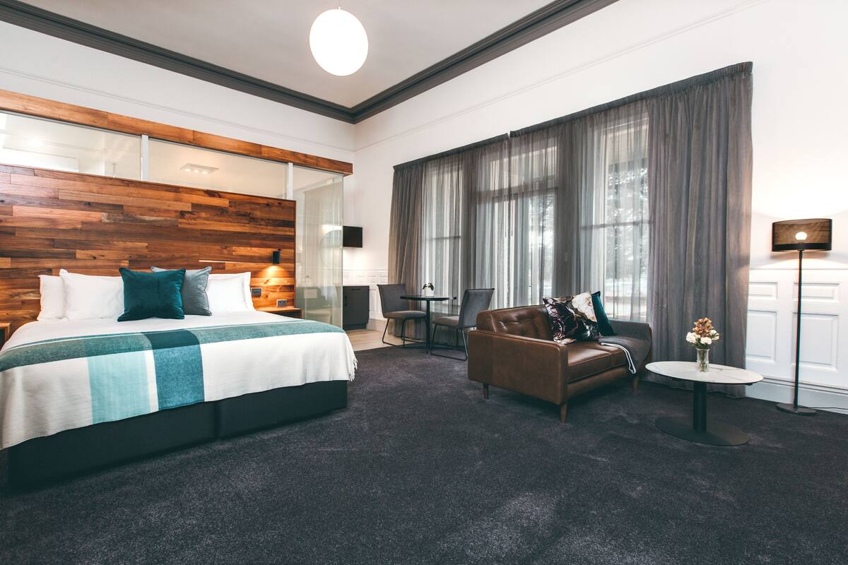 A modern hotel room with a large bed, a leather sofa, a small table, and a desk.