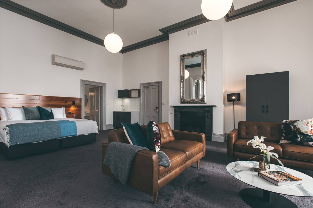 A hotel room with a bed, two sofas, a fireplace, and a round coffee table.