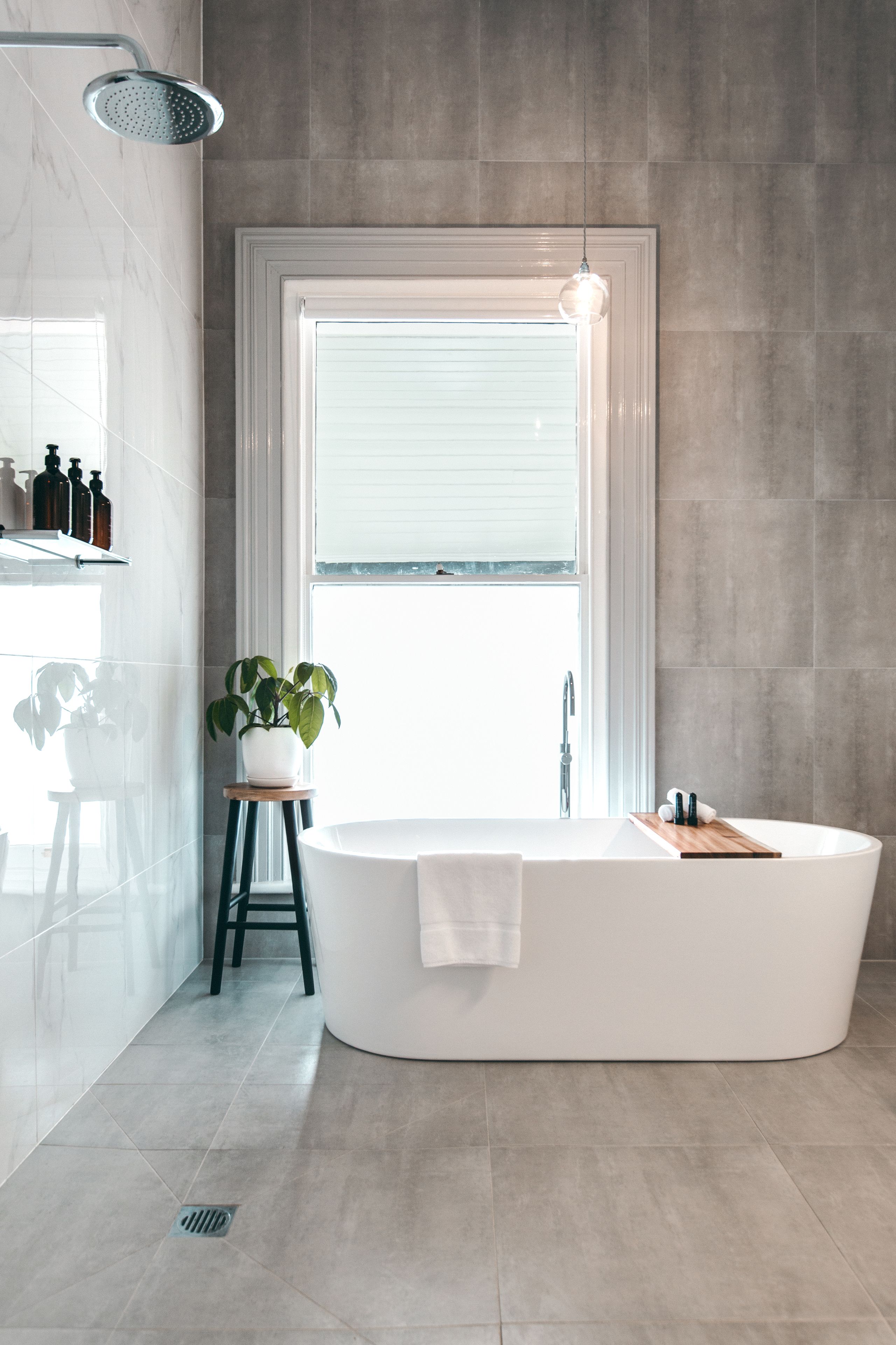 Een moderne badkamer met een vrijstaand bad, een plant in pot en een raam dat natuurlijk licht binnenlaat.