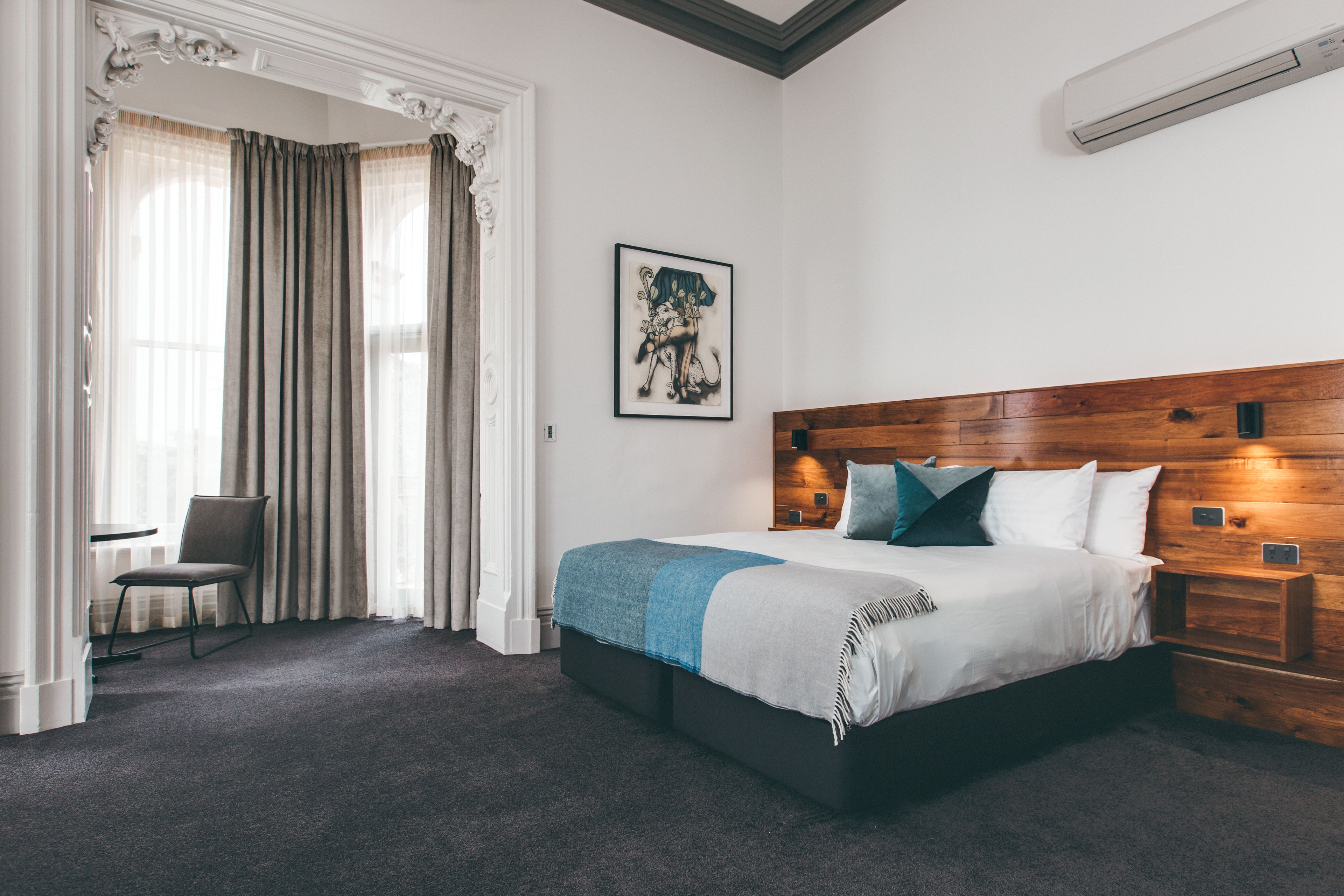 Une chambre à coucher avec un grand lit, une tête de lit en bois, une chaise et une fenêtre avec des rideaux.