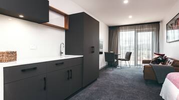A modern hotel room with a kitchenette, a dining area, and a bed.
