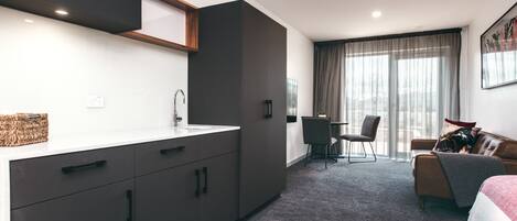 A modern hotel room with a kitchenette, a dining area, and a bed.