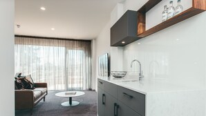 A modern kitchen with a white countertop, a built-in oven, and a wooden shelf above the sink. - Maylands Lodge (New Town)