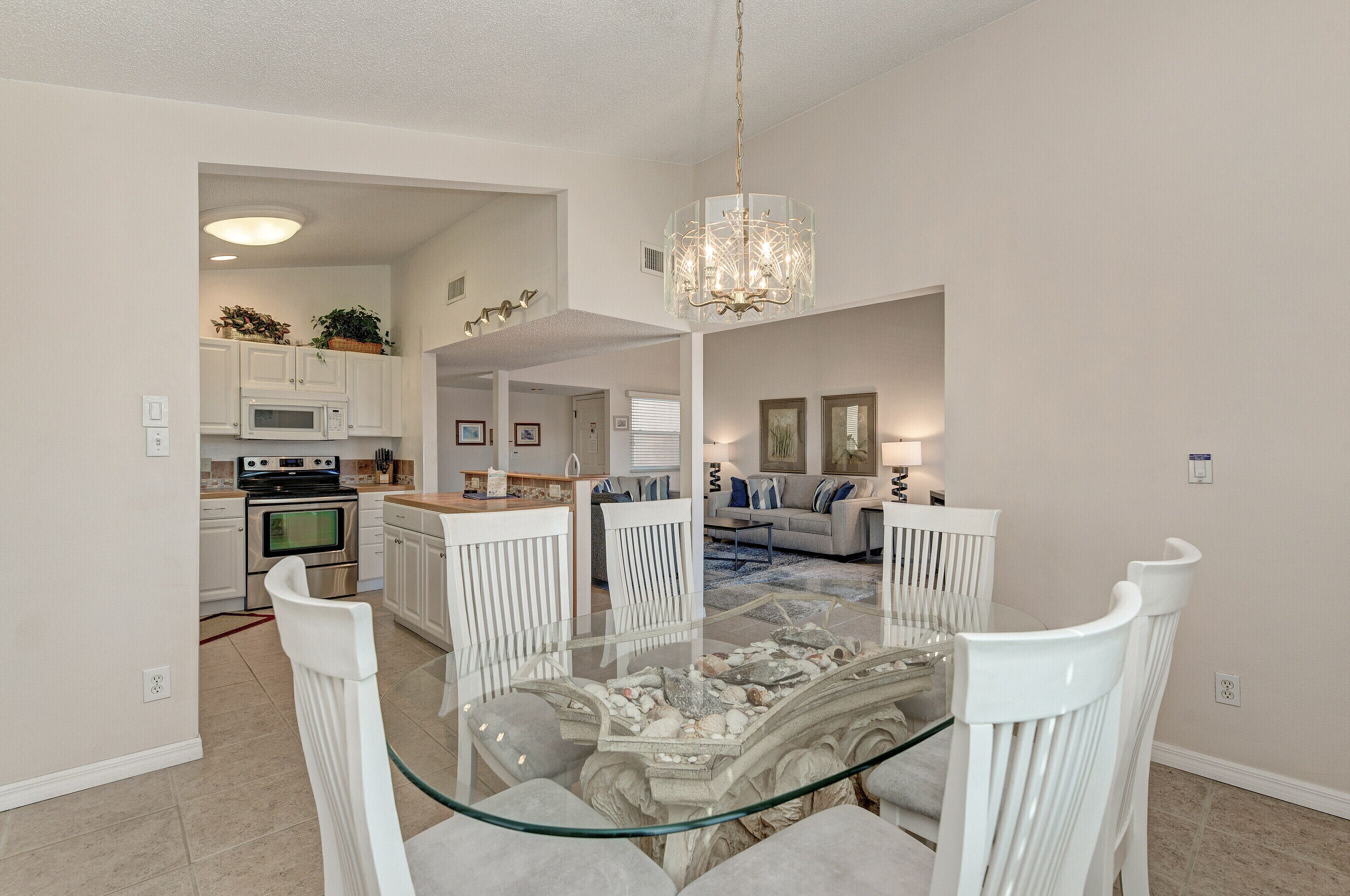 A modern kitchen with white cabinets, a microwave, and a stove. There is a dining area with a glass table and white chairs.