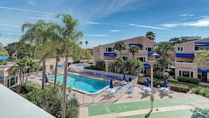 A hotel with a swimming pool, lounge chairs, and a tennis court.