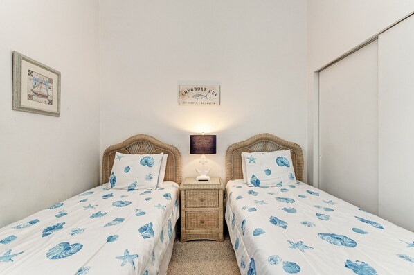 A bedroom with two single beds, a nightstand with a lamp, a framed map on the wall, and a small wooden chest.