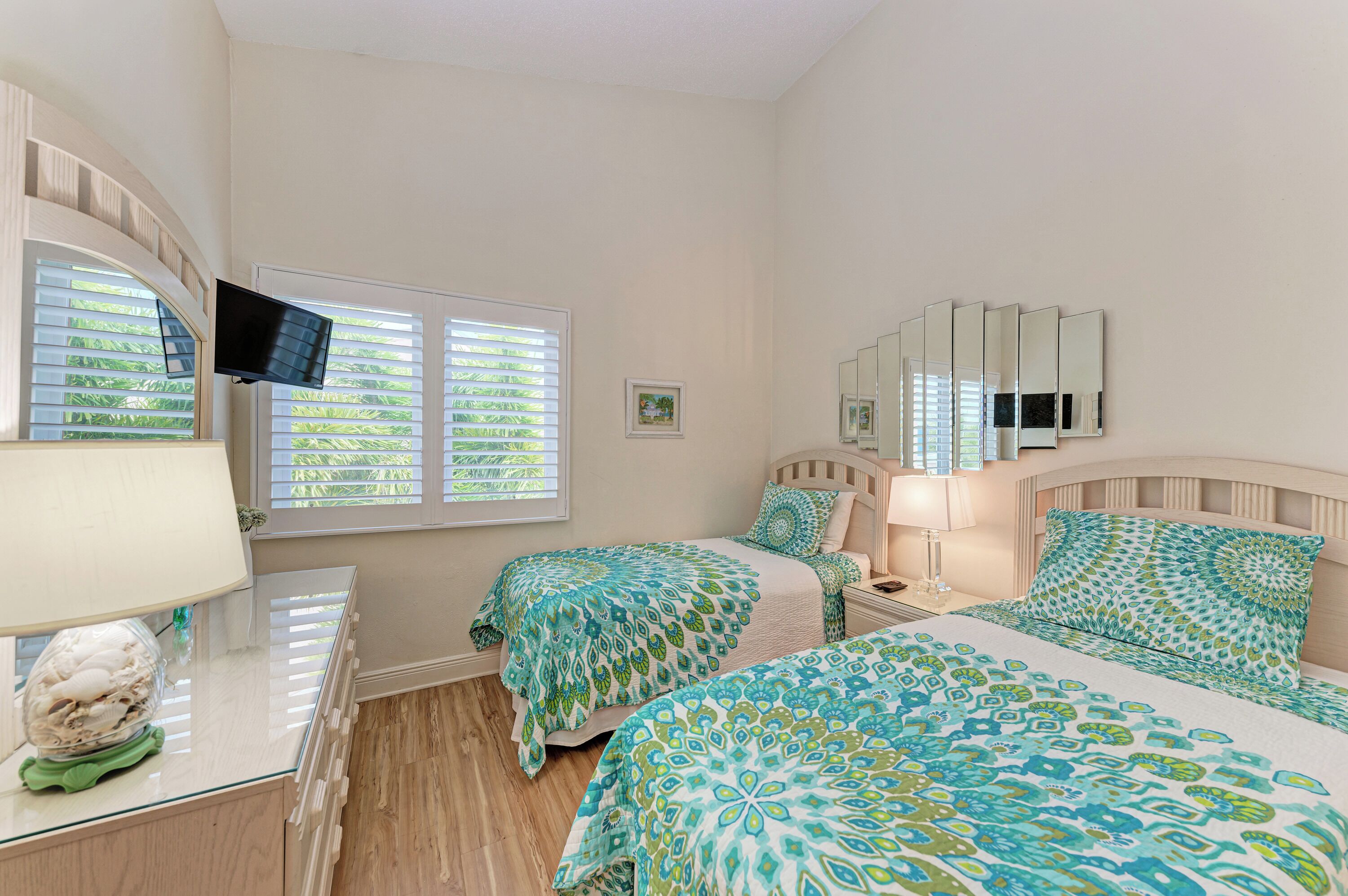 A bedroom with two beds, a TV, a mirror, and a window with blinds.
