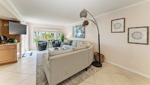 A modern living room with a sofa, a flat-screen TV, a dining area, and a kitchen.