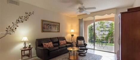 A living room with a black sofa, a round coffee table, a floor lamp, and a ceiling fan.