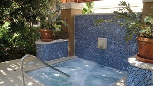 Ein Whirlpool mit einer mosaikverzierten Wand, umgeben von Topfpflanzen.