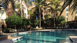 Ein Pool, umgeben von Palmen und Liegestühlen, mit einem Gebäude im Hintergrund.