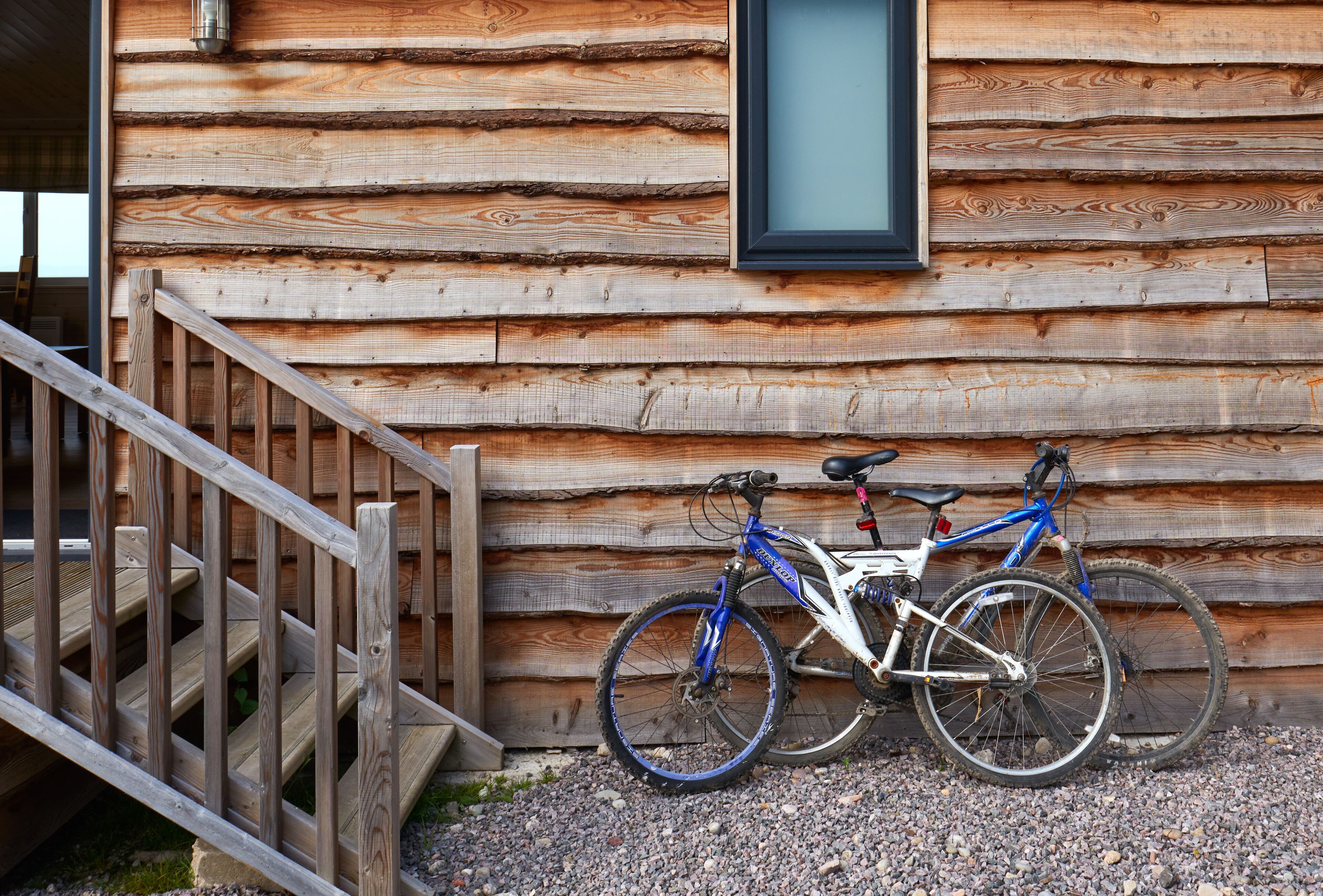 A wooden cabin with a wooden staircase leading to a door. A bicycle is parked against the cabin wall.