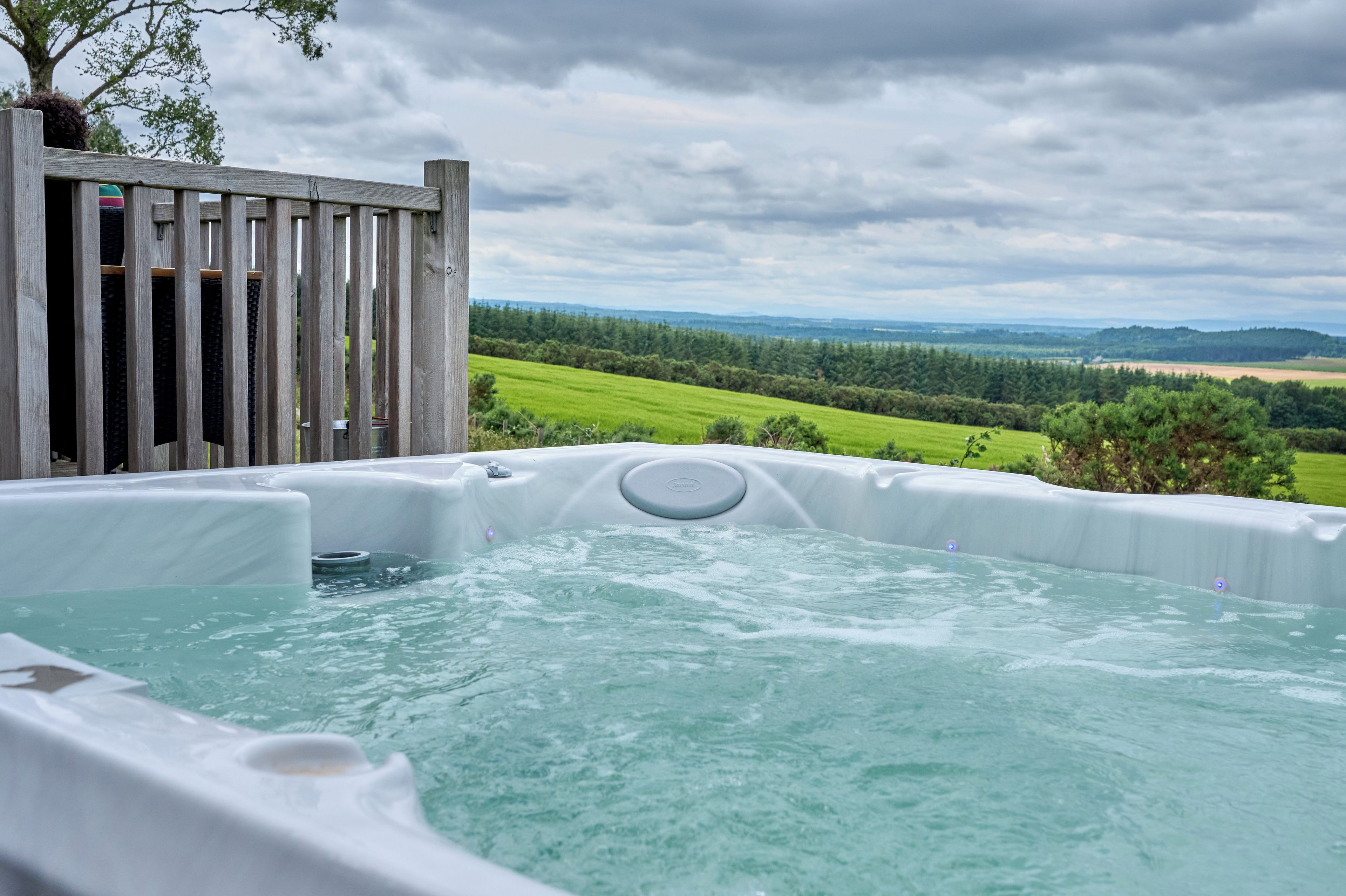 A hot tub with a wooden deck and a scenic view of a green landscape.
