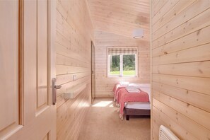 A wooden cabin room with a bed, a window, and a door. - 2-bed Woodland Lodge with private hot tub and expansive views. (Forres)