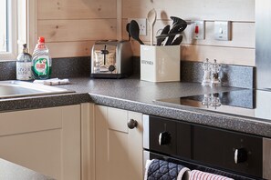A kitchen with a granite countertop, a toaster, a spice rack, and a sink. - 2-bed Woodland Lodge with private hot tub and expansive views. (Forres)