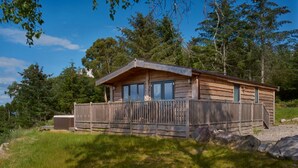 A wooden cabin with a balcony, surrounded by trees and a clear sky. - 2-bed Woodland Lodge with private hot tub and expansive views. (Forres)