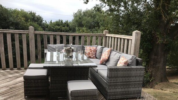 Patio esterno con divano in vimini, tavolino in vetro e pouf coordinati.