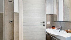 Un baño moderno con cabina de ducha de vidrio, un lavabo blanco sobre tocador de madera y un espejo grande sobre el lavabo.