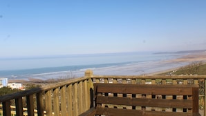 A wooden bench overlooking a beach with a clear view of the ocean and distant buildings. - Old Saltys Cottage in Westward Ho with stunning sea views (Northam)
