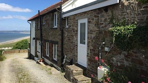 A stone building with a white door and a small porch. - Old Saltys Cottage in Westward Ho with stunning sea views (Northam)