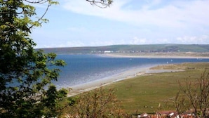 A coastal landscape with a beach, grassy areas, and a distant shoreline. - Old Saltys Cottage in Westward Ho with stunning sea views (Northam)