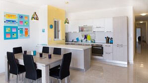 Cozinha moderna com ilha central, armários brancos e área de refeições com cadeiras pretas.