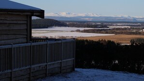 Une cabane en bois avec une rambarde en métal, un paysage enneigé et des montagnes lointaines.