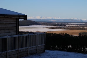 A wooden cabin with a metal railing, a snowy landscape, and distant mountains. - Cosy woodland retreat with private hot tub. Pet-friendly! (Forres)