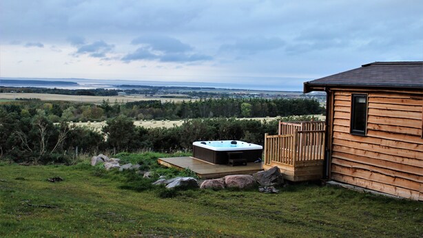 Une cabane en bois dotée d’un bain à remous et d’une terrasse offrant une vue imprenable sur un paysage magnifique.