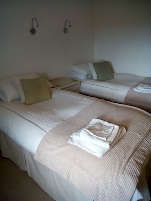 Habitación de hotel con dos camas, cada una con almohada, manta y toalla doblada. Hay dos lámparas fijadas a la pared.