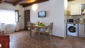 Une cuisine compacte équipée d’un lave-linge, d’une table à manger avec des chaises et d’un téléviseur fixé au mur.