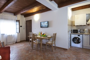 A compact kitchen with a washing machine, a dining table with chairs, and a television mounted on the wall.