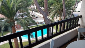 A balcony with a view of a swimming pool, palm trees, and a street.