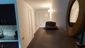A narrow hallway with a wooden floor, a round mirror on the right, and a door at the end.