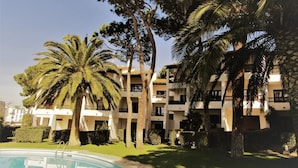 A hotel with a swimming pool, palm trees, and a well-maintained garden.