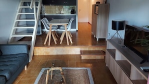 A modern living room with a sofa, a coffee table, a TV, and a staircase leading to a dining area with chairs and a table.
