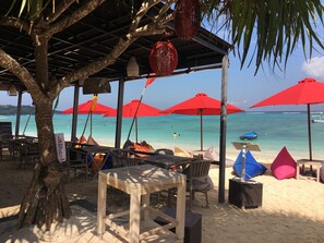 Ein Café am Strand mit Außenplätzen, roten Sonnenschirmen und Blick auf das Meer.