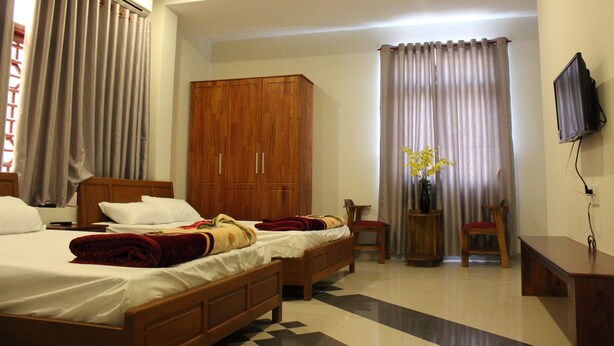 A hotel room with two beds, a wooden wardrobe, a small desk with a chair, and a TV mounted on the wall.