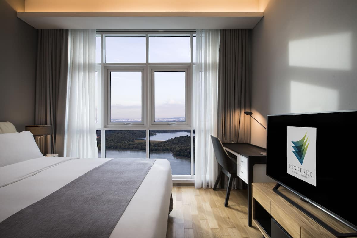 A hotel room with a large bed, a desk, and a TV displaying the Pine Tree Marina Resort logo.