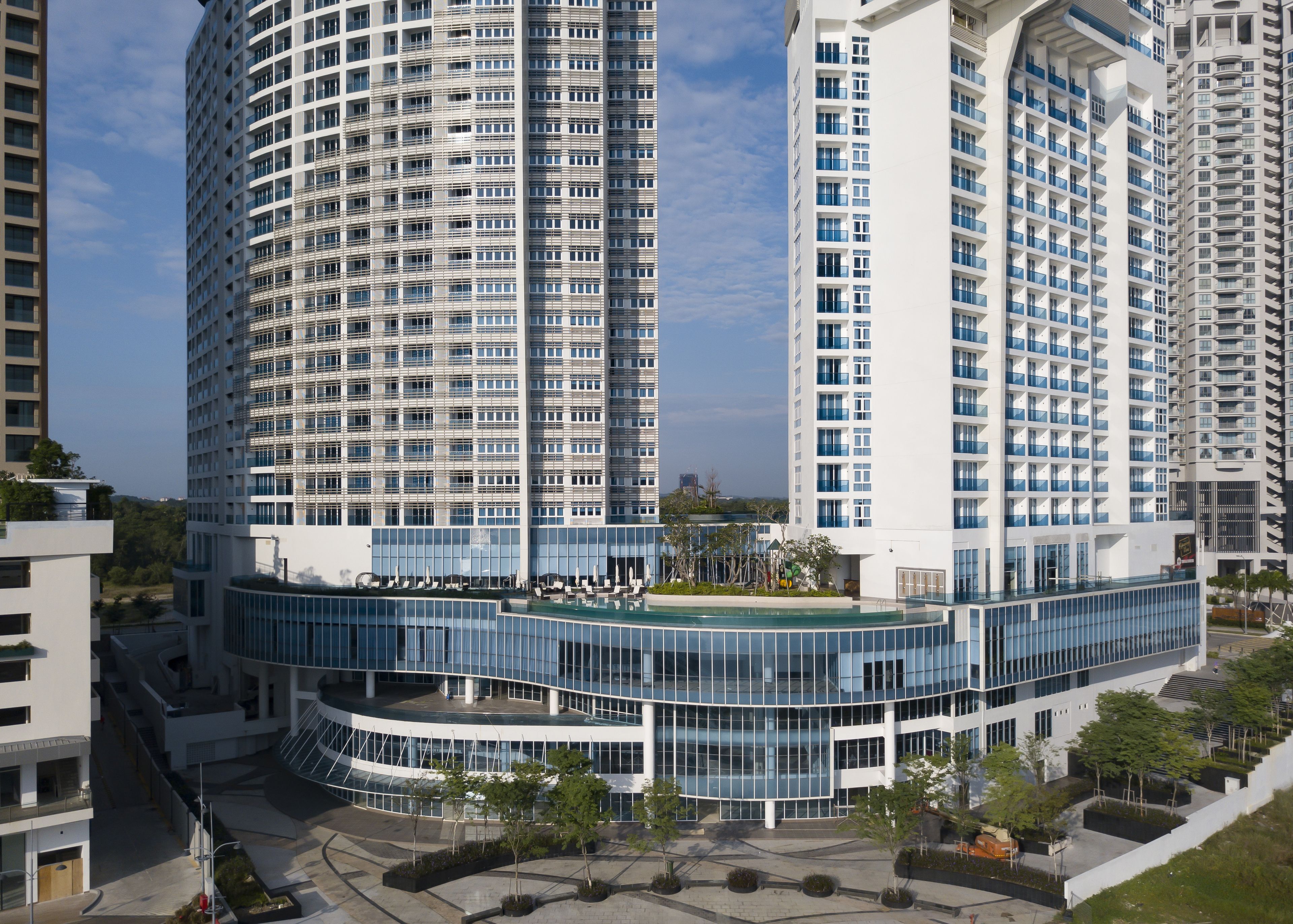 A modern high-rise building with a curved glass facade, multiple balconies, and a rooftop terrace.
