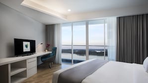 Habitación de hotel moderna con una cama grande, un escritorio con computadora, una silla y un ventanal con vistas a una masa de agua.