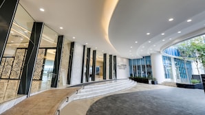 Una entrada de hotel moderna con techo curvo, puertas de cristal y una escalera de mármol que conduce al vestíbulo.