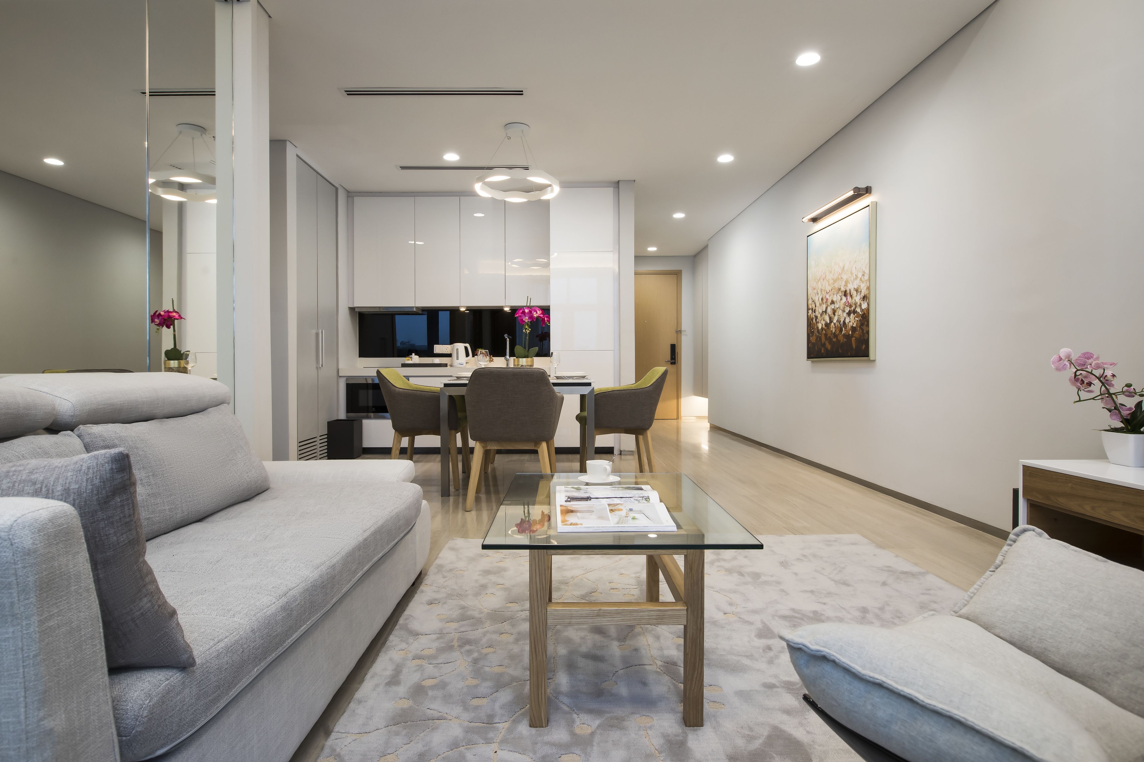 A modern living room with a glass coffee table, grey sofas, and a dining area with chairs and a table.