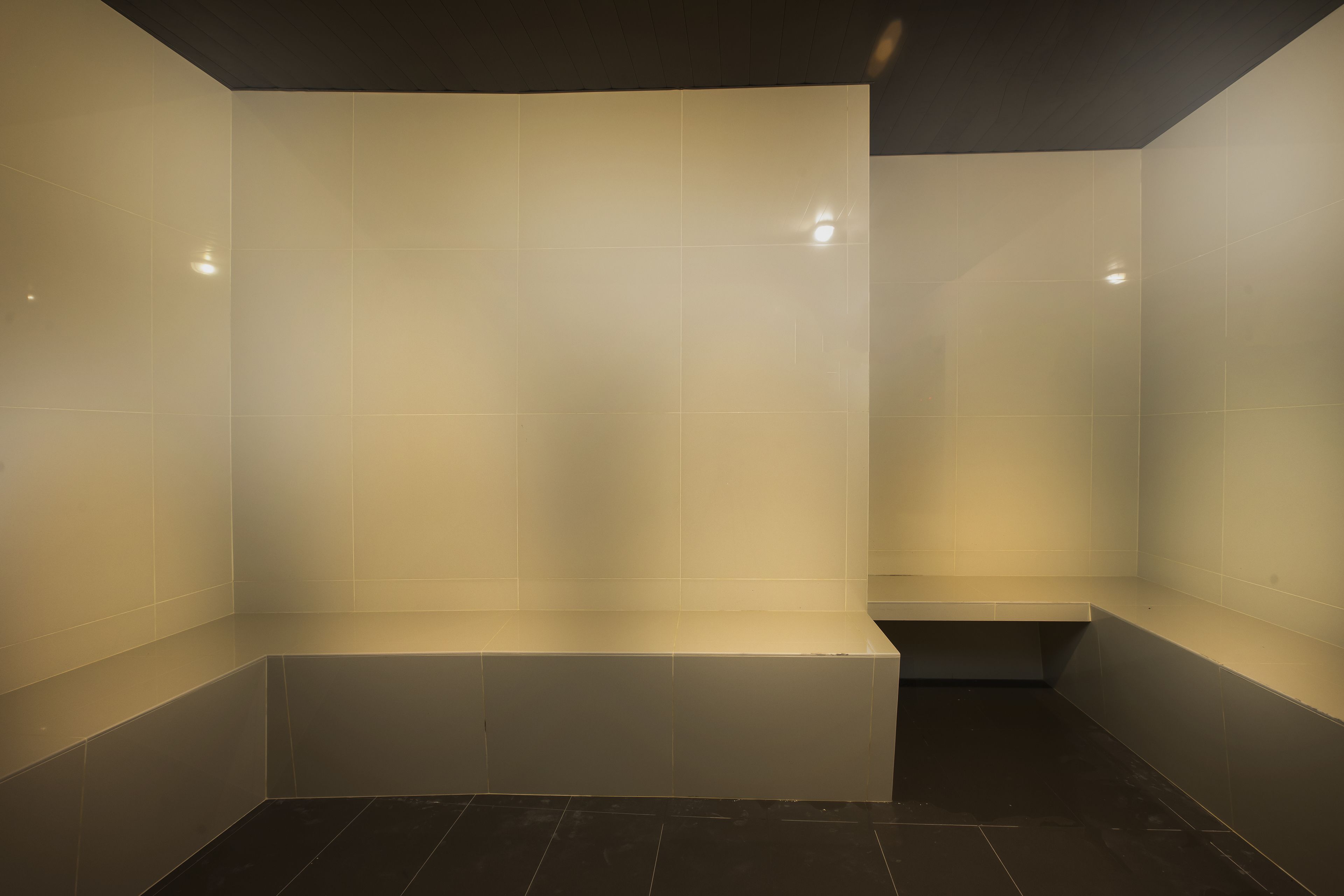 A modern bathroom with white tiles, a bench, and a dark floor.