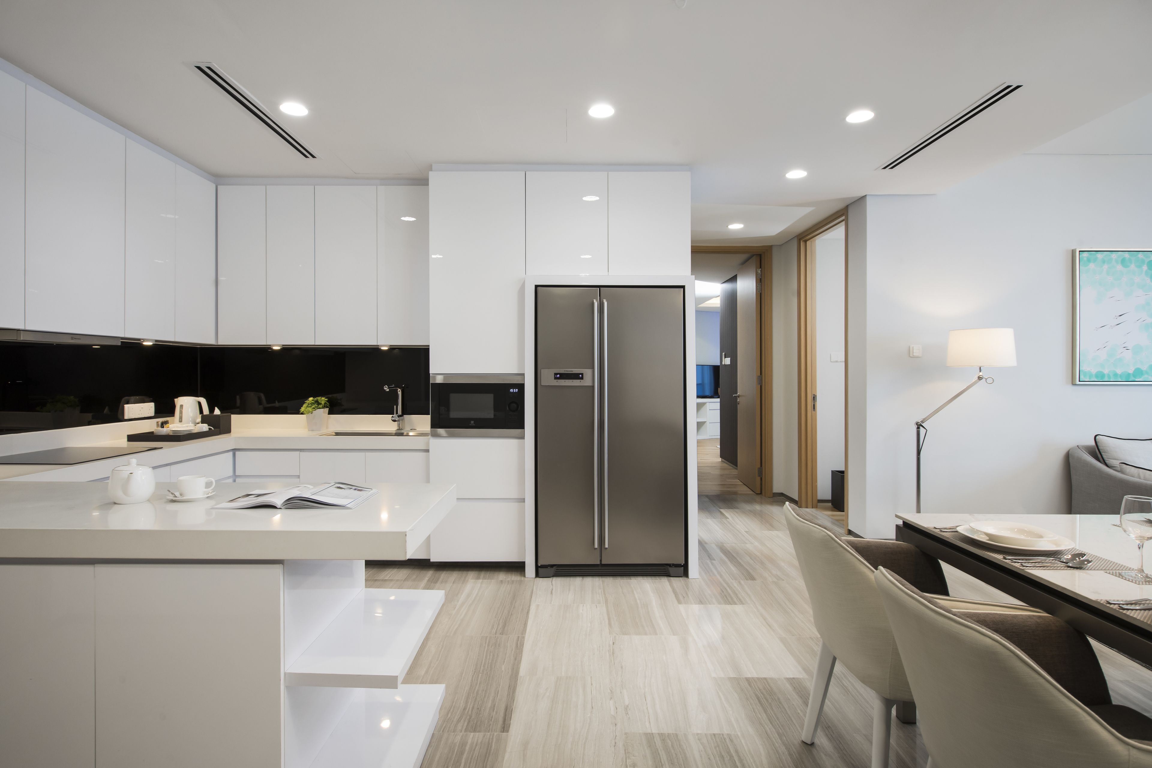 A modern kitchen with white cabinetry, a stainless steel refrigerator, and a dining area with a table and chairs.
