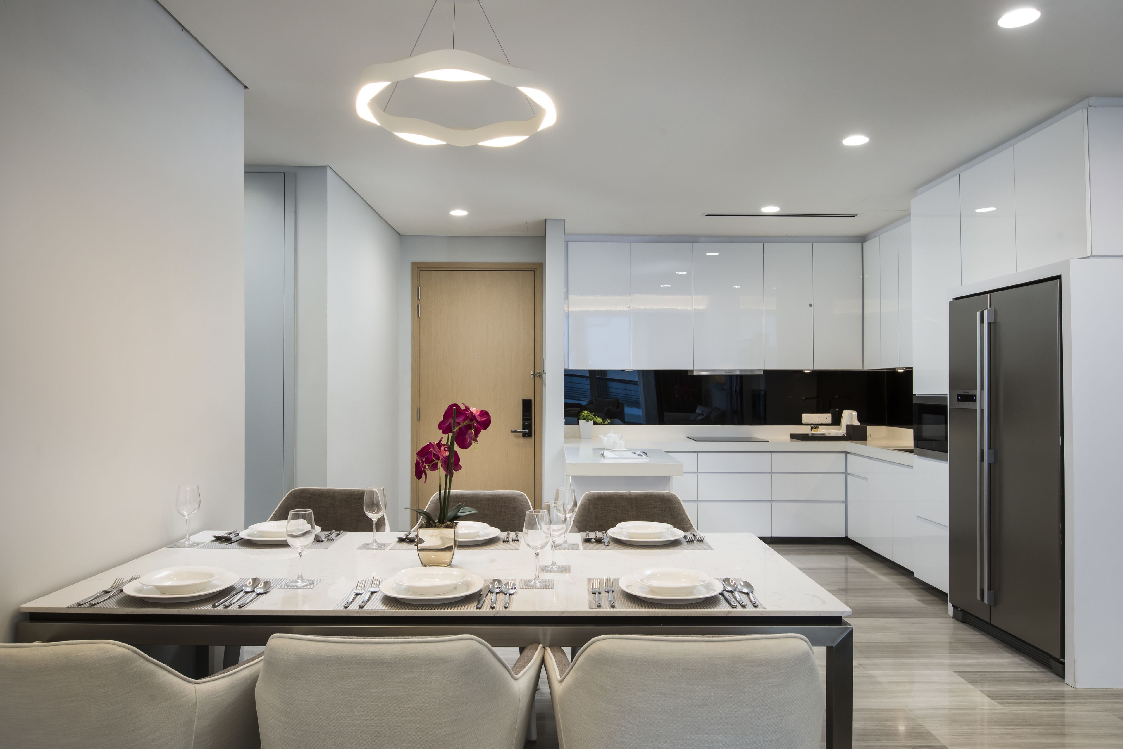 A modern kitchen with white cabinets, a stainless steel refrigerator, and a dining area with a table set for four.